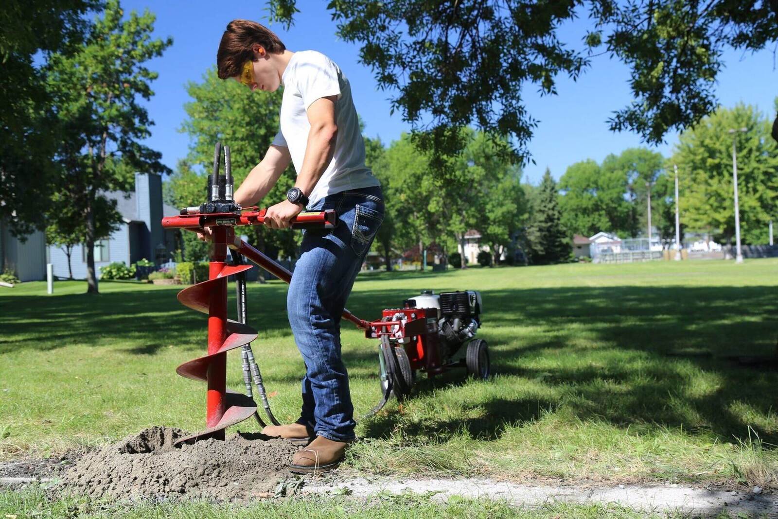 Little Beaver hydraulic earth drill in use as a man drills a post hole in a field